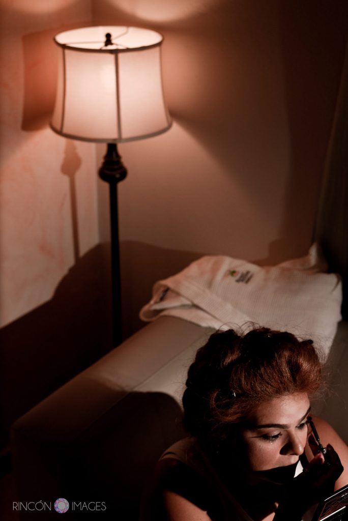 Bride doing her eye makeup by a pink lamp in the living room.