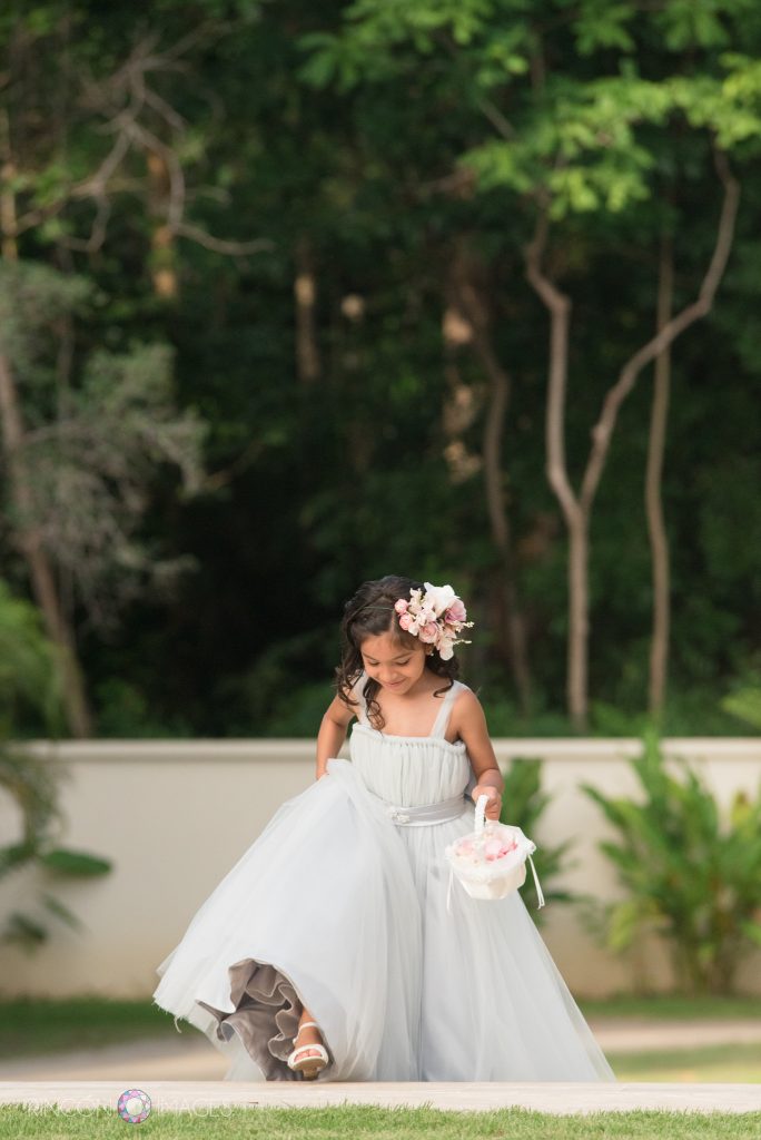 A flower girl wearing a grey dress takes a step up the staircase to start processing to the front of the wedding ceremony.