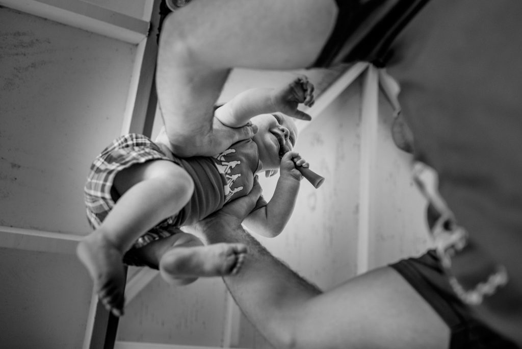 Low angle photograph of a father holding his baby in the air.