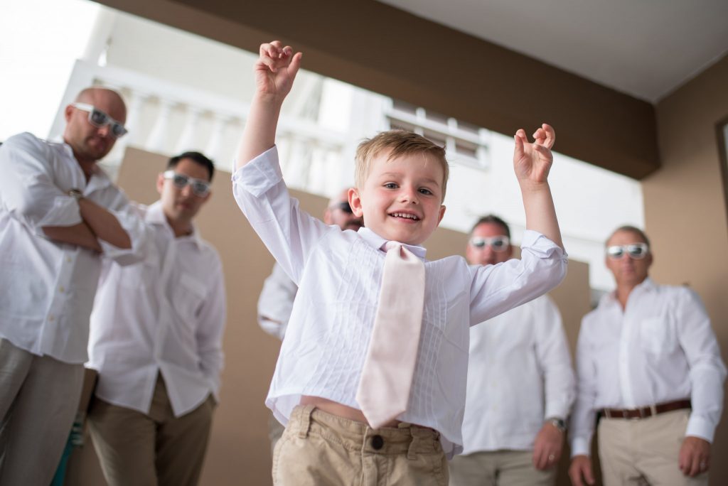 Children at weddings looking cute in a pink tie and white shirt in front of a line of groomsmen.