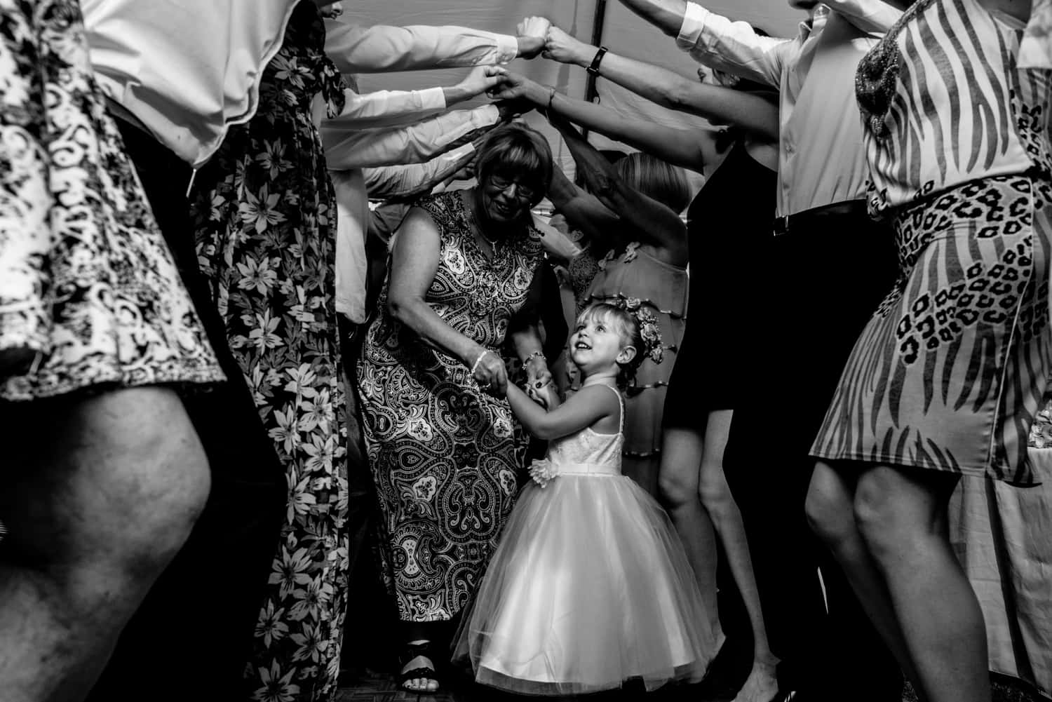 Flower girl under a bunch of arms dancing during a wedding reception.