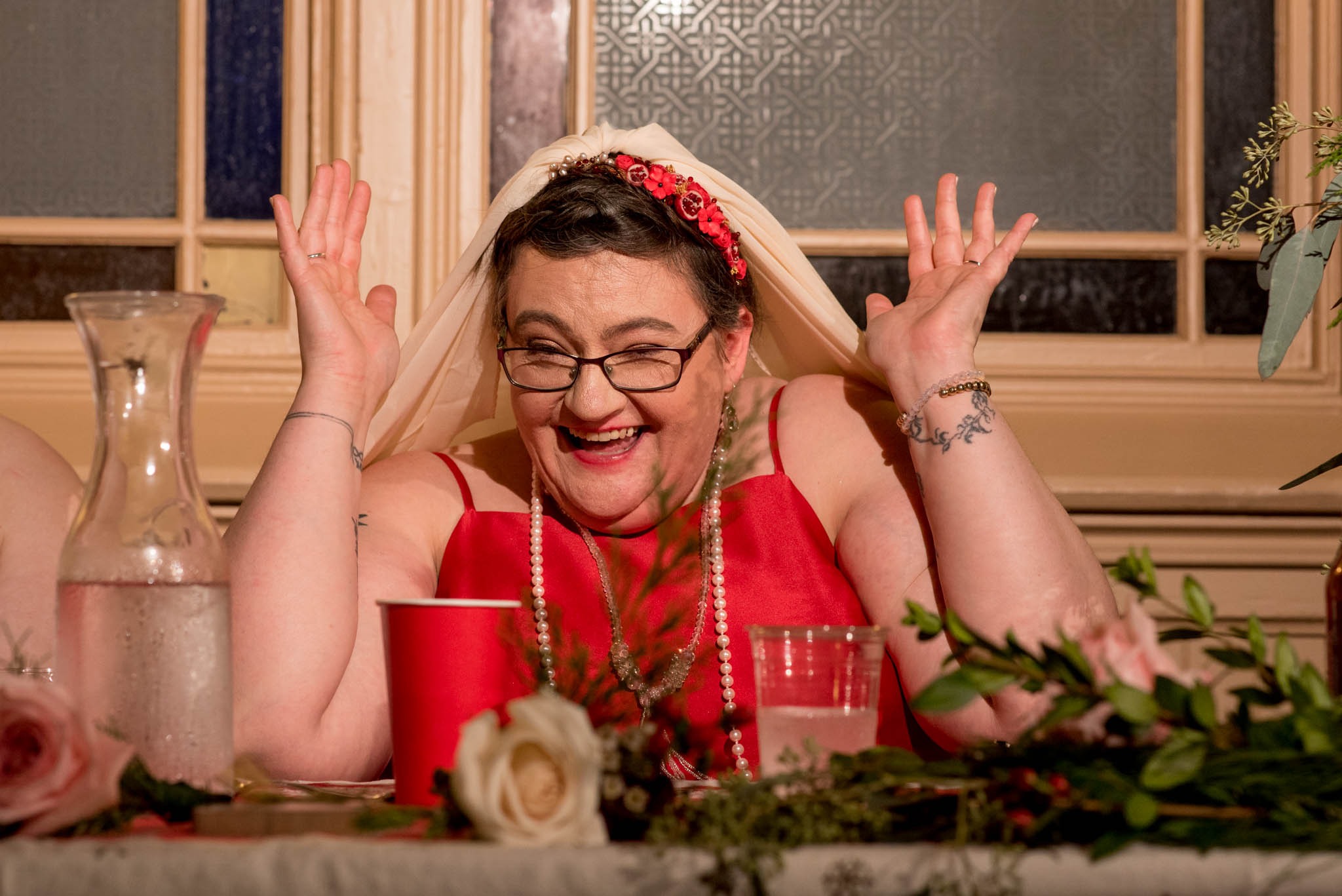 Bride wearing red dress laughing during wedding reception toasts