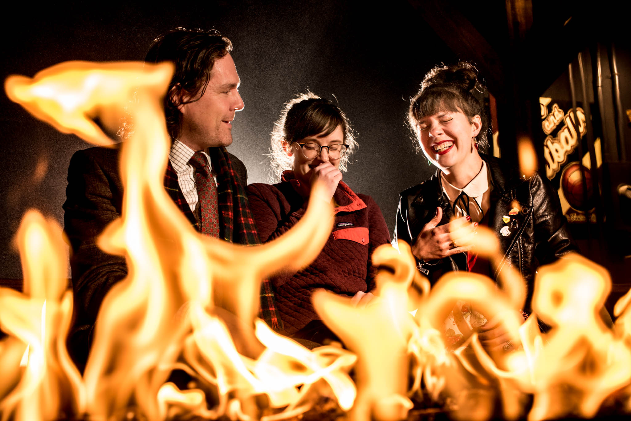 Three wedding guests laughing in front of a fire pit
