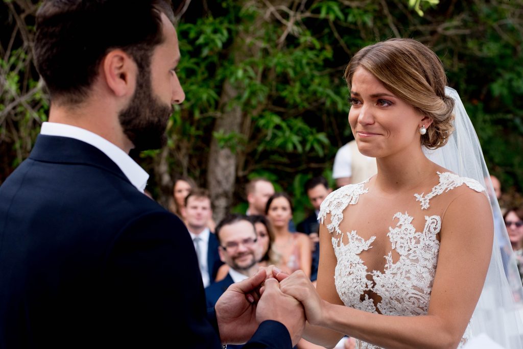 Bride holding hands with her groom while crying during their wedding ceremony