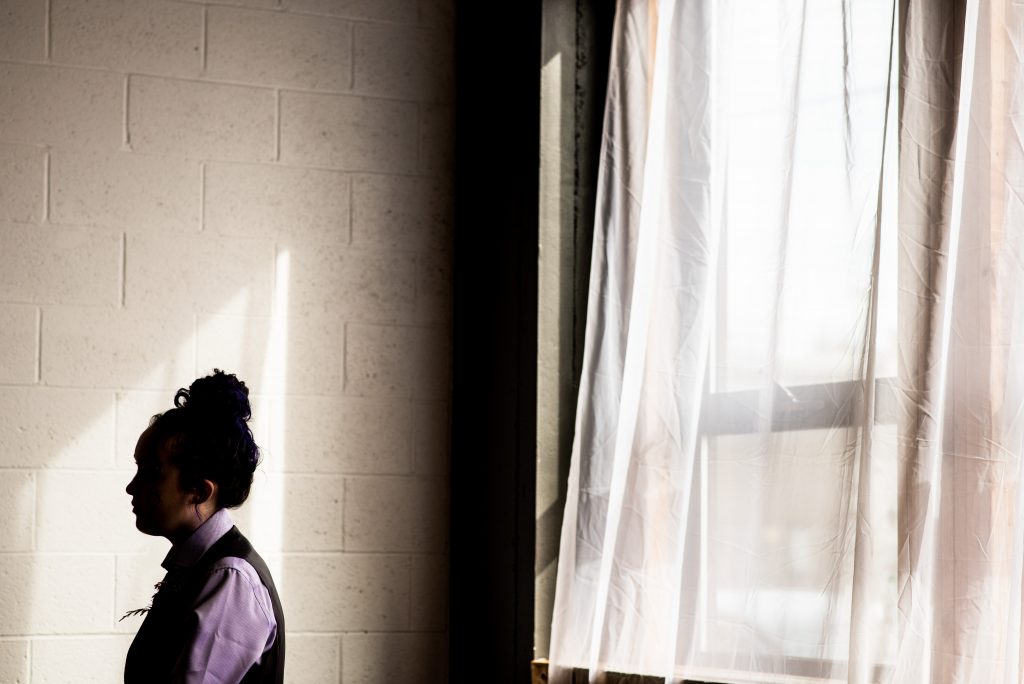 silhouette of bridesmaid wearing purple in front of a white wall.
