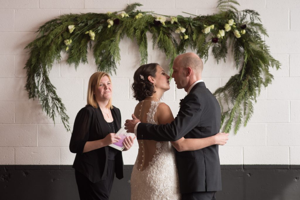Bride and groom kissing in front of pine wedding decorations