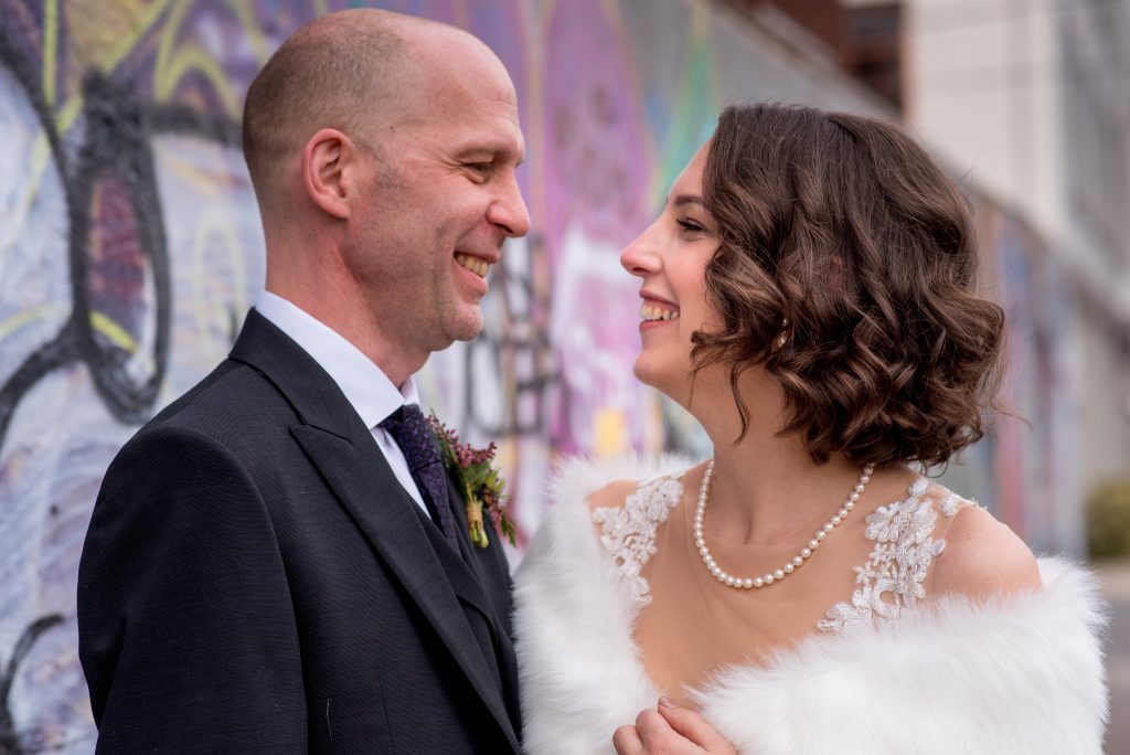 Bride and groom looking at each other in front of graffiti wall.