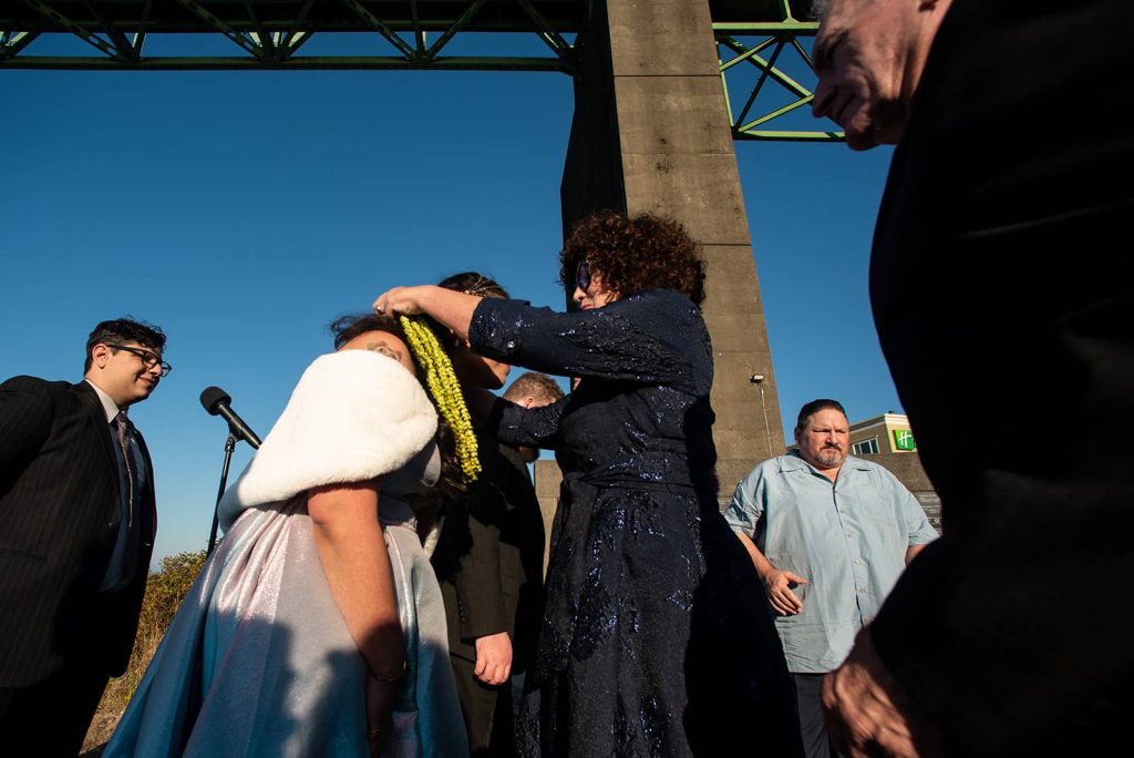 A family member of the bride and groom puts green flower leis on the bride at The Maritime Memorial Park during the ceremony.