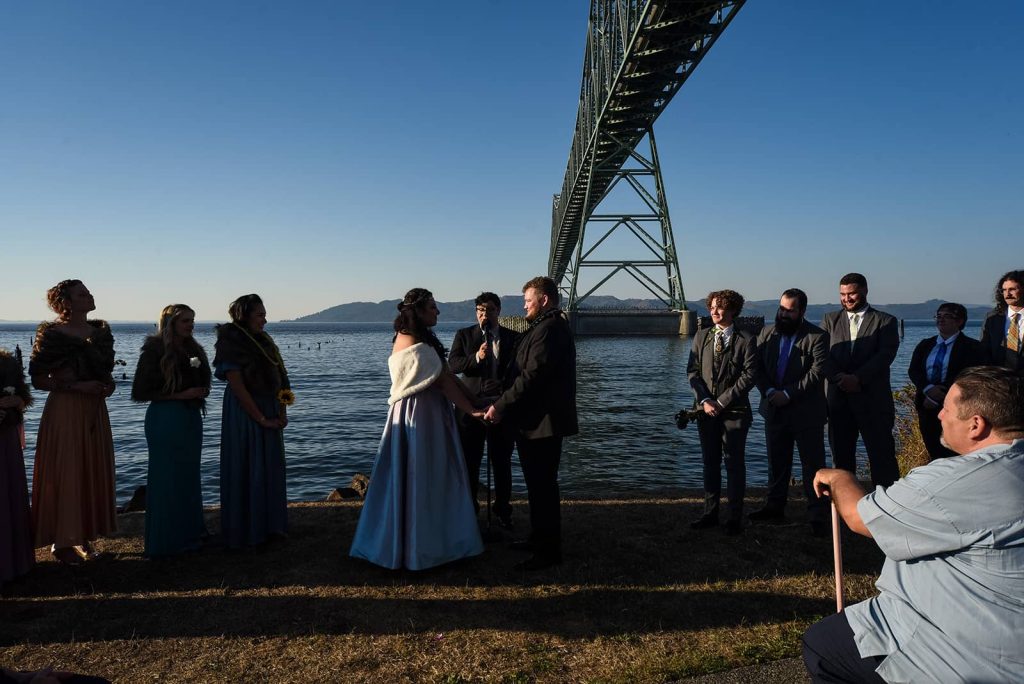 The groom and bride stand under a bridge by the waters during the ceremony with family members at The Maritime Memorial Park.