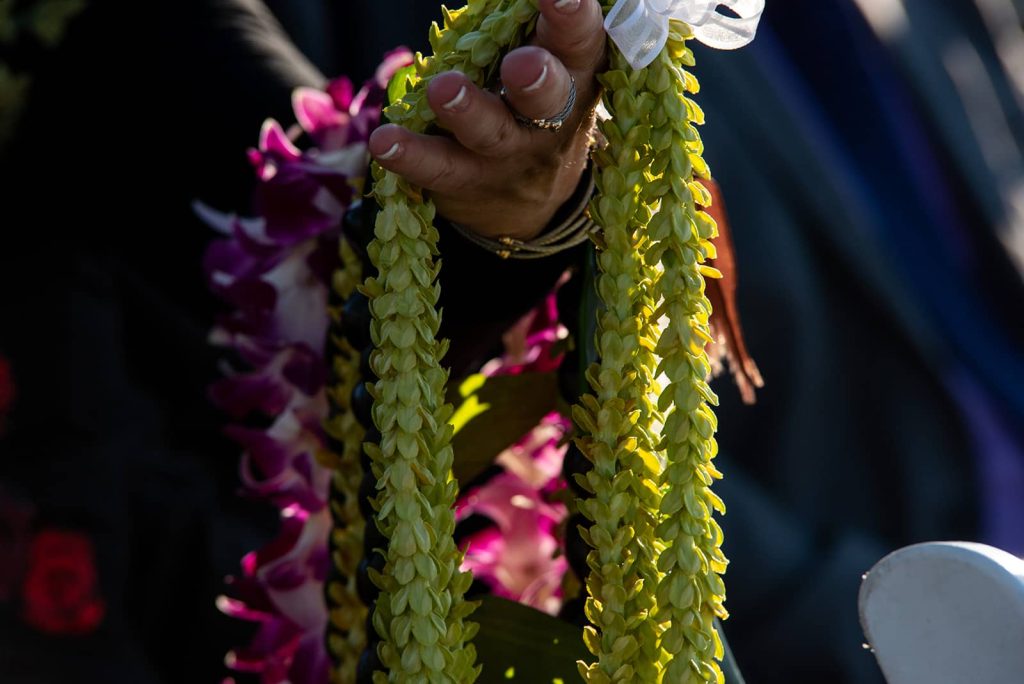 Hand of a wedding guest holding green flower and purple orchid flower leis at The Maritime Memorial Park during the ceremony.