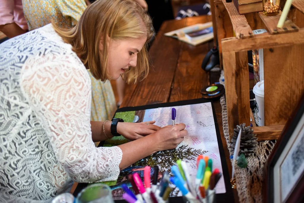 A wedding guest signing a completed puzzle artwork on the table at the reception at The Loft at The Red Building in Astoria, Oregon.