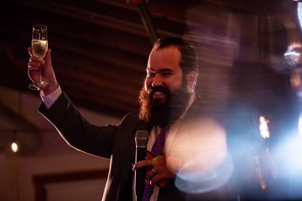 A groomsman is raising his glass to propose a toast to the bride and groom at the reception at The Loft at The Red Building in Astoria, Oregon.