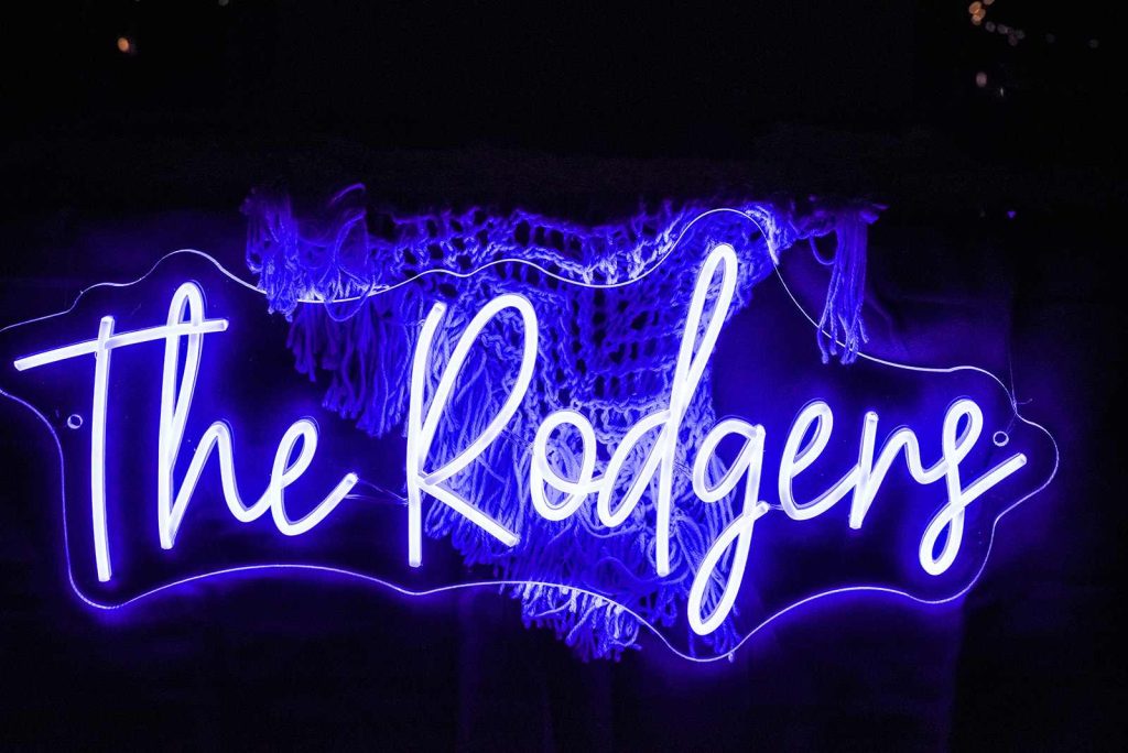 Blue neon sign that reads “The Rodgers” featured at a wedding reception.