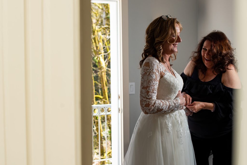 a woman helping another woman put on her wedding dress.