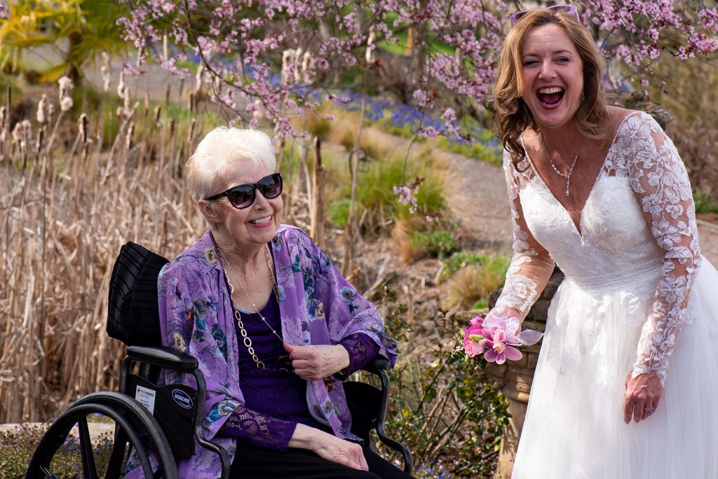 a woman in a wheelchair laughing next to a woman in a wedding dress.