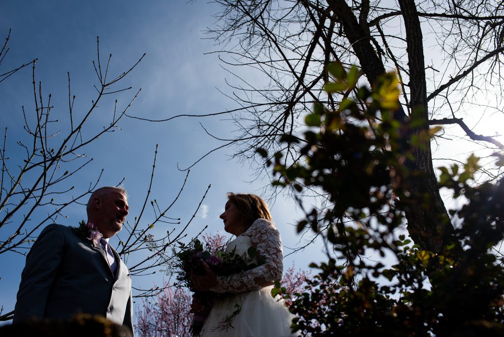 a man and a woman standing next to each other with trees in the background and a blue sky
